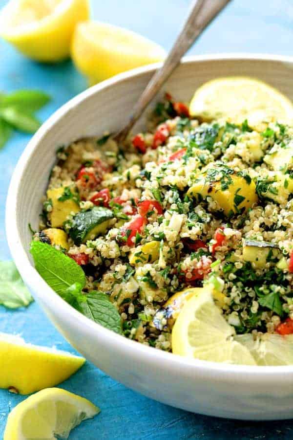 Photo of Quinoa Tabbouleh with Grilled Vegetables garnished with mint spring and lemon wedges in white serving bowl.