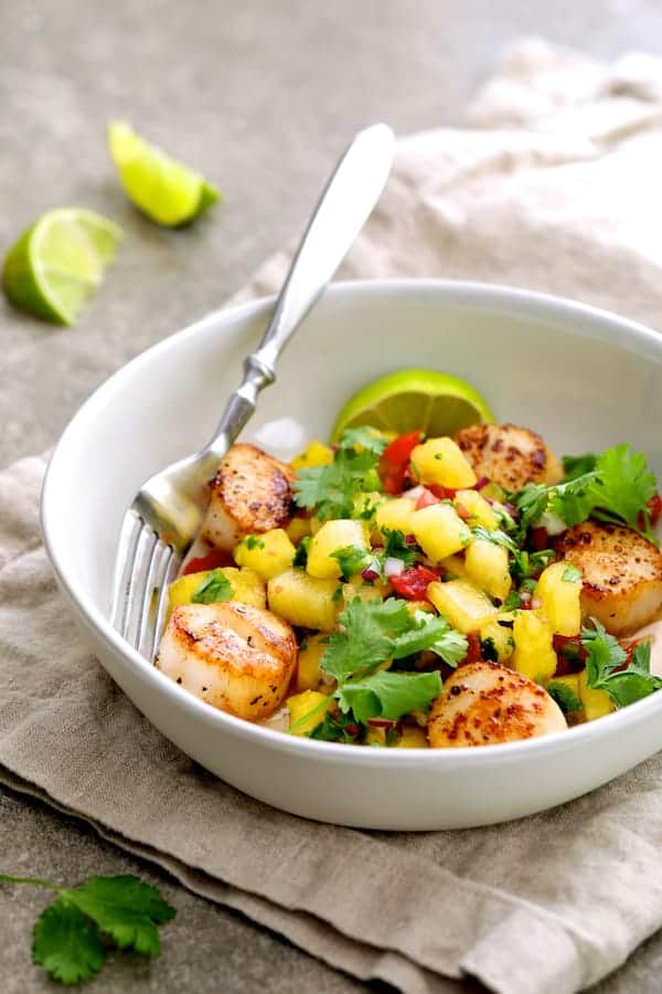 Photo of Seared Sea Scallops with Watermelon Tomato Salsa in white bowl on beige napkin garnished with cilantro and lime wedges.