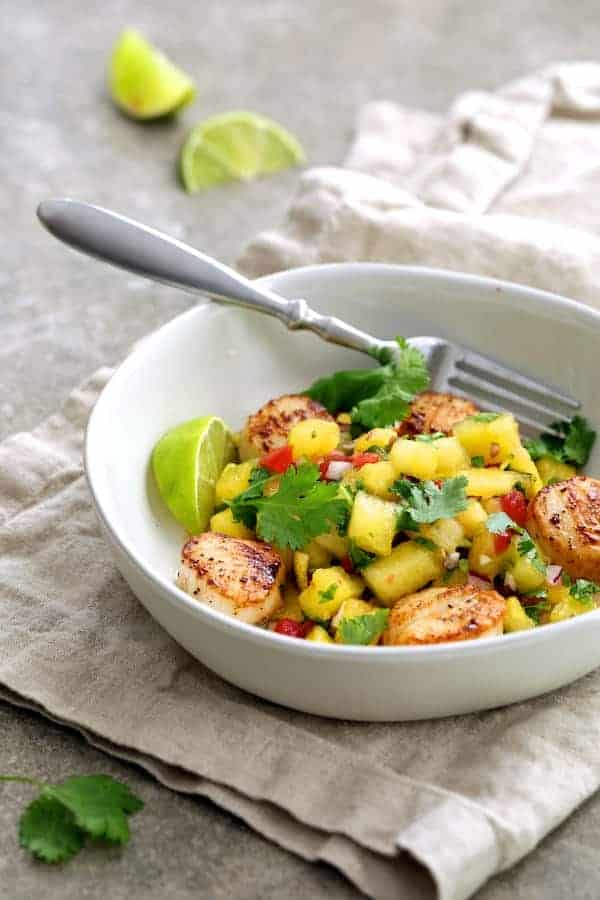 Photo of Seared Sea Scallops with Watermelon Tomato Salsa in white bowl garnished with cilantro and lime wedges.