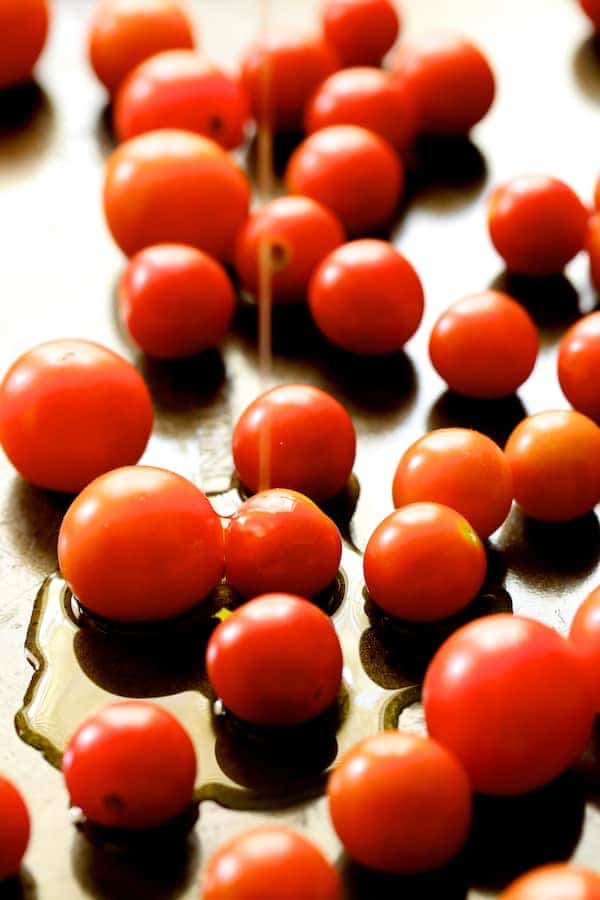 Photo of cherry tomatoes on baking sheet being drizzled with olive oil.