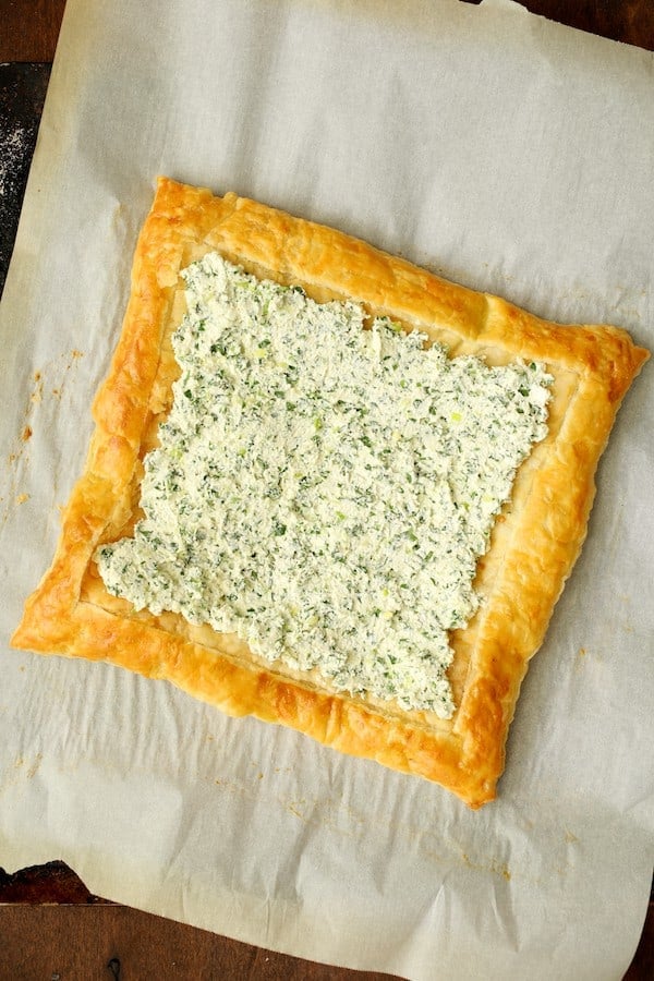 Photo of baked puff pastry crust on parchment paper with ricotta mixture spread over it.