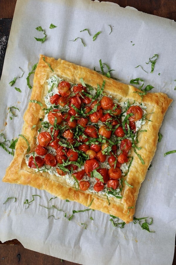 Photo of tart on parchment paper with basil sprinkled over the top.