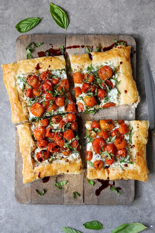Photo of Roasted Cherry Tomato Tart with Herbed Ricotta on wood cutting board cut into four pieces.