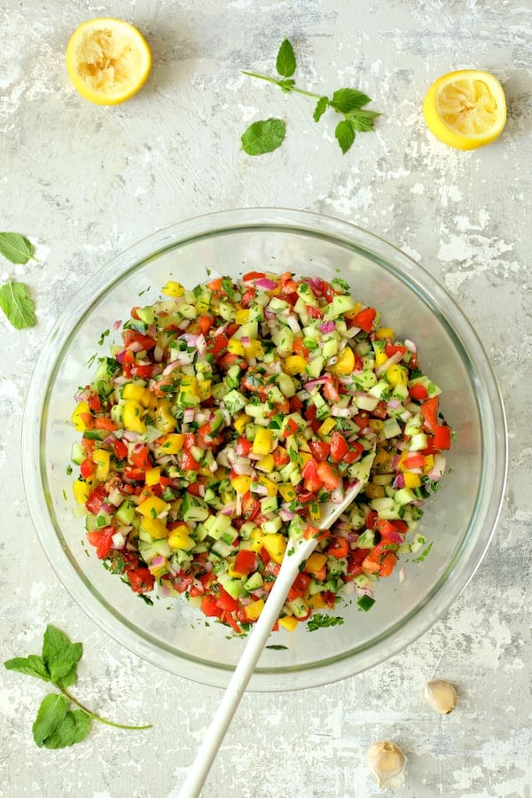Photo of salad in glass mixing bowl after being stirred with white mixing spoon.