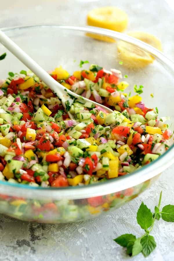 Photo of Middle Eastern Vegetable Salad in glass mixing bowl after being stirred with white mixing spoon.
