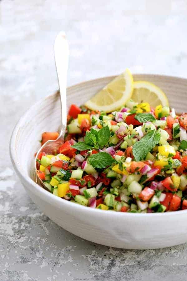Photo of Middle Eastern Vegetable Salad in a white bowl garnished with mint sprigs and lemon slices.