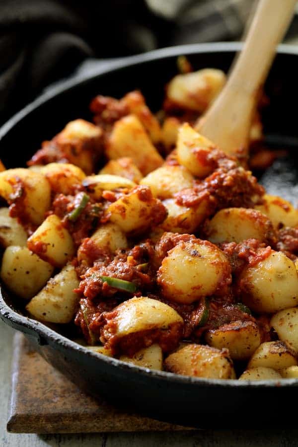 Close-up photo of potatoes being stirred with sauce in cast iron skillet with wooden spoon.