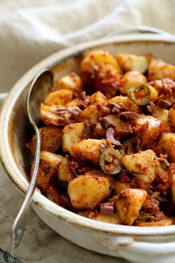 Close-up photo of Patatas Bravas Chilenos in clay bowl with serving spoon.