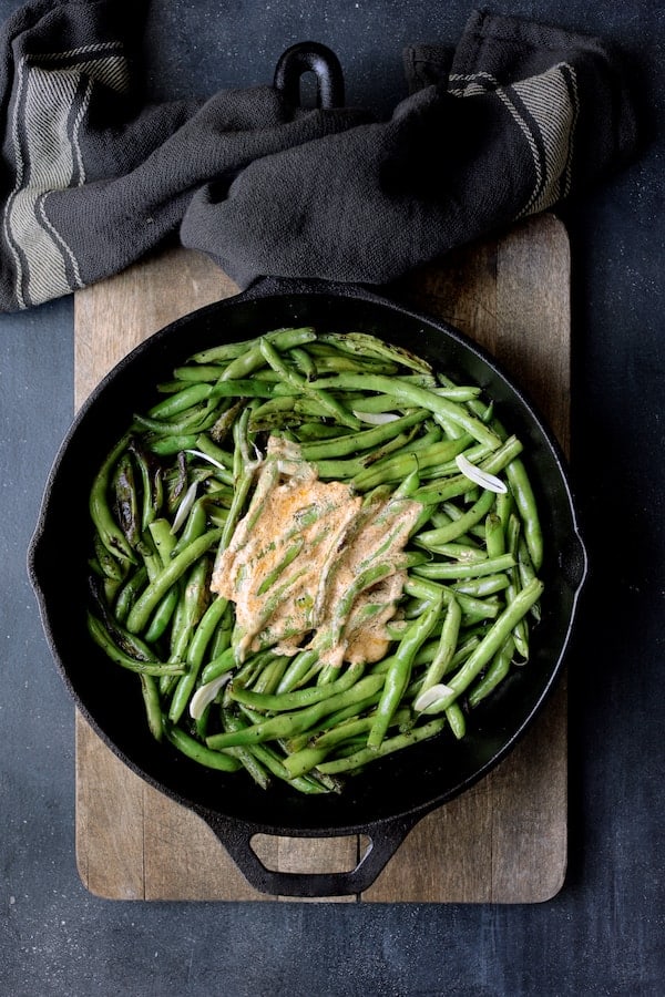 Photo of Skillet Charred Green Beans with Goat Cheese Chipotle Butter in cast iron skillet on wood cutting board.