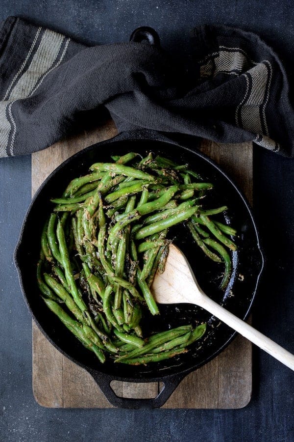Photo of Skillet Charred Green Beans with Goat Cheese Chipotle Butter in cast iron skillet being stirred with wooden spoon.