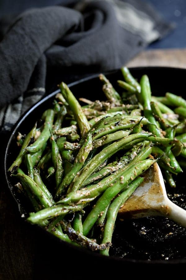 Photo of Skillet Charred Green Beans with Goat Cheese Chipotle Butter in cast iron skillet being stirred with wooden spoon.