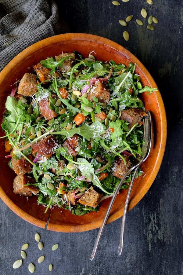 Photo of Autumn Panzanella Salad in wood bowl with serving utensils.