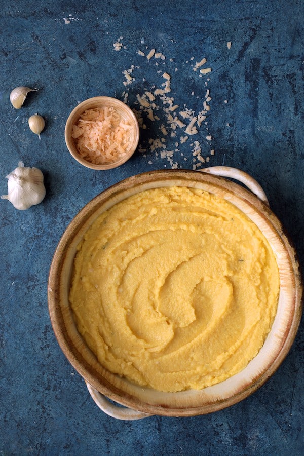 Photo of polenta layer cooling/setting up in round earthenware baking dish on blue background.