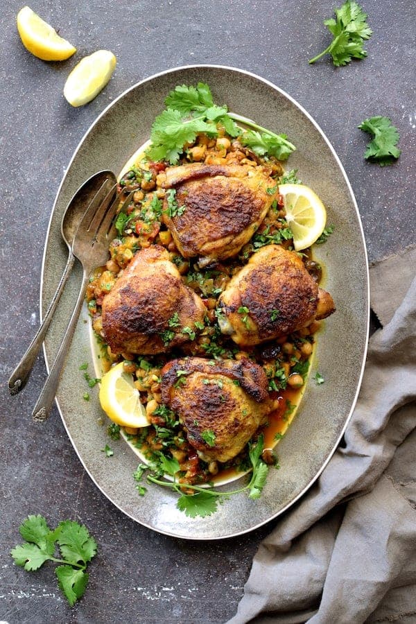 Photo of Moroccan Chicken Tagine with Butternut Squash Chickpeas and Olives on gray-rimmed platter garnished with cilantro and lemon wedges.