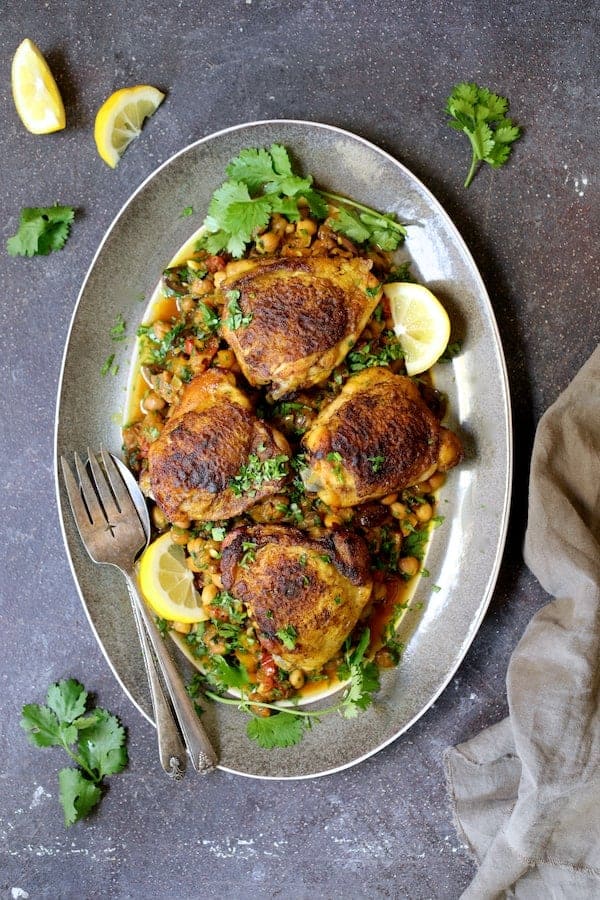 Photo of Moroccan Chicken Tagine with Butternut Squash Chickpeas and Olives on gray-rimmed platter garnished with lemon wedges and cilantro.