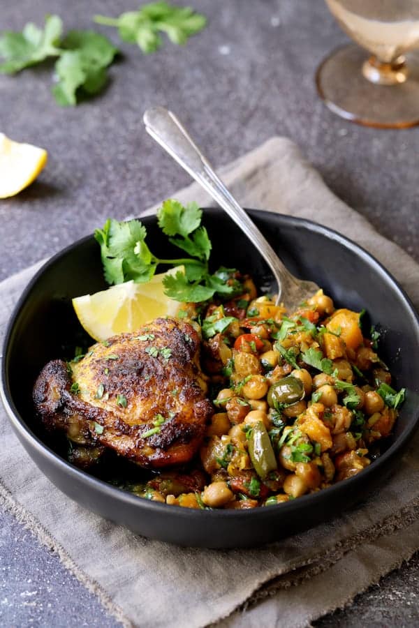 Photo of one serving of Moroccan Chicken Tagine with Butternut Squash, Chickpeas and Olives in black bowl.