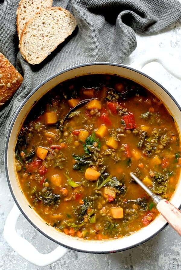 Spicy Kale, Butternut Squash and Lentil Soup with Bacon in a white enamel cast iron Dutch oven with soup ladle.