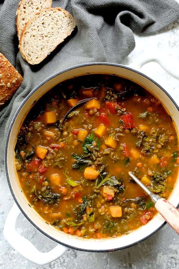 Photo of Spicy Kale Butternut Squash and Lentil Soup with Bacon in white Dutch oven.