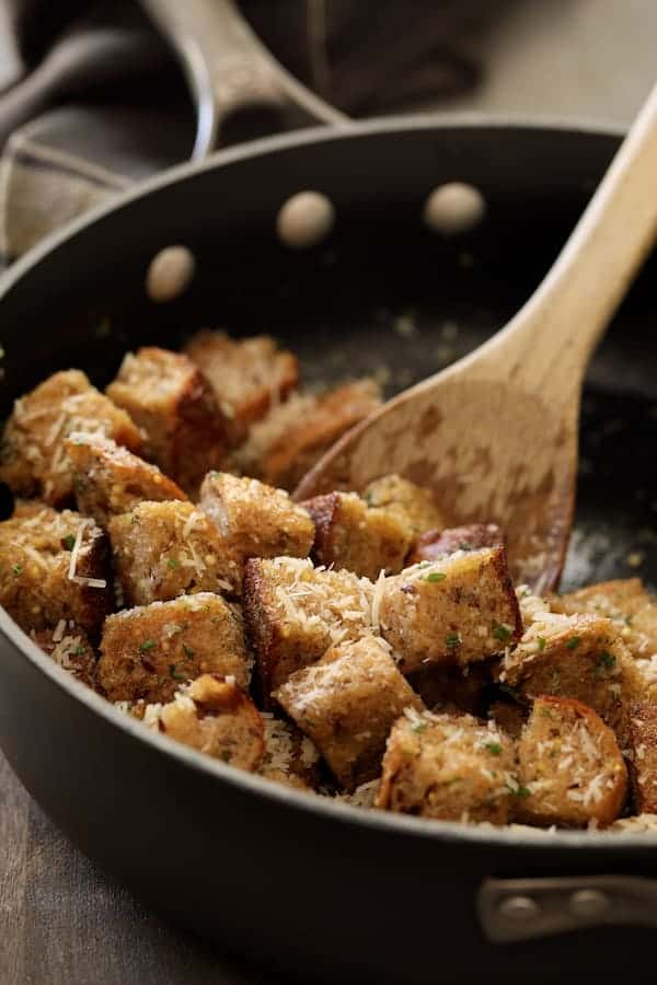 Photo of bread cubes in saute pan being stirred with wooden spoon.
