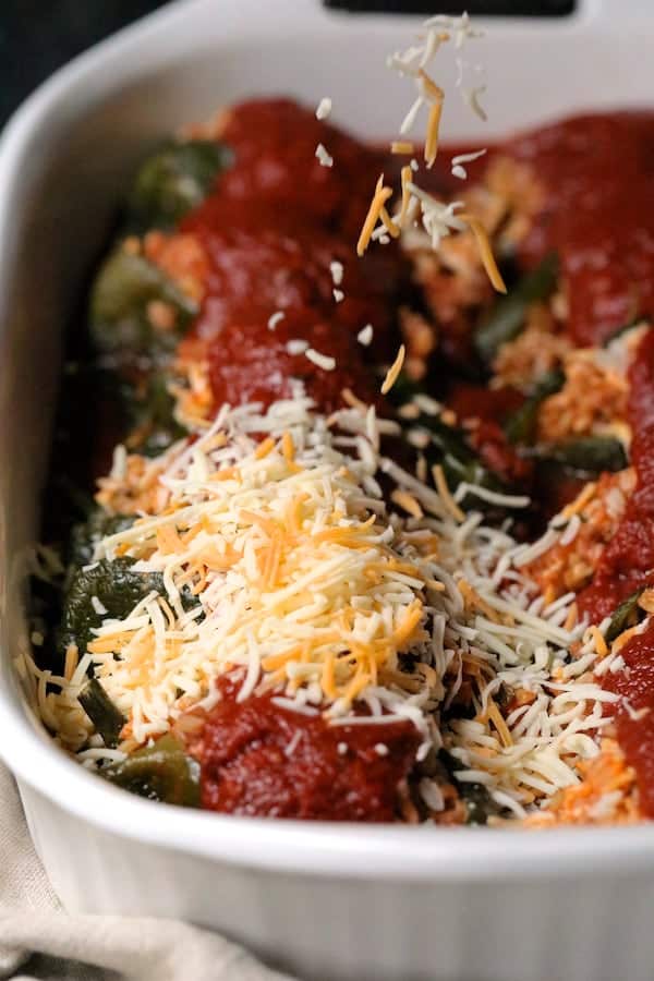 Photo of cheese being sprinkled over sauced peppers.