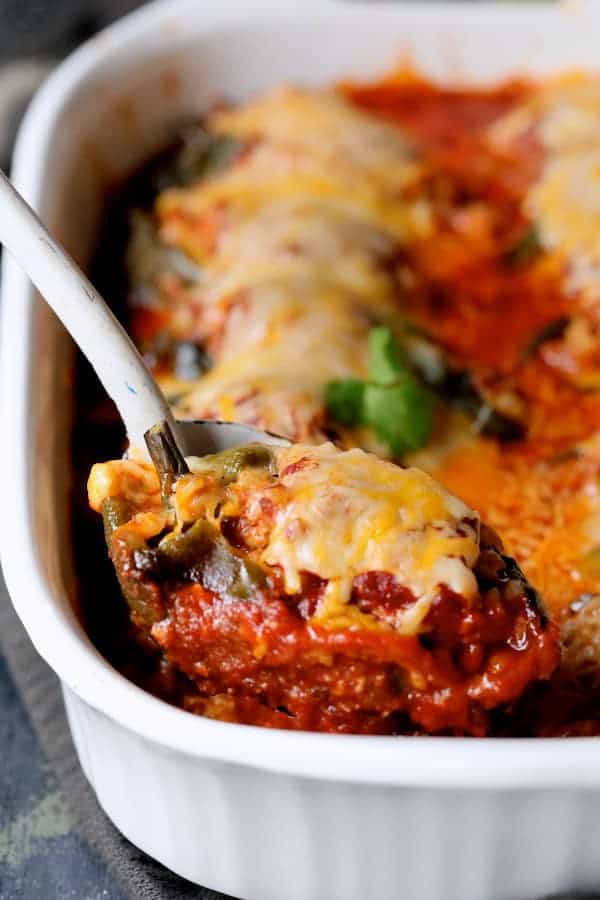 Photo of Chorizo and Brown Rice Stuffed Poblano Peppers with one poblano being scooped from baking dish with white spoon.