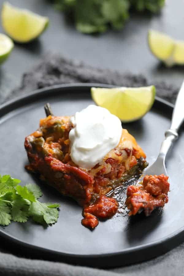 Photo of one serving of Chorizo and Brown Rice Stuffed Poblano Peppers on black plate garnished with lime wedge, cilantro and dollop of sour cream.