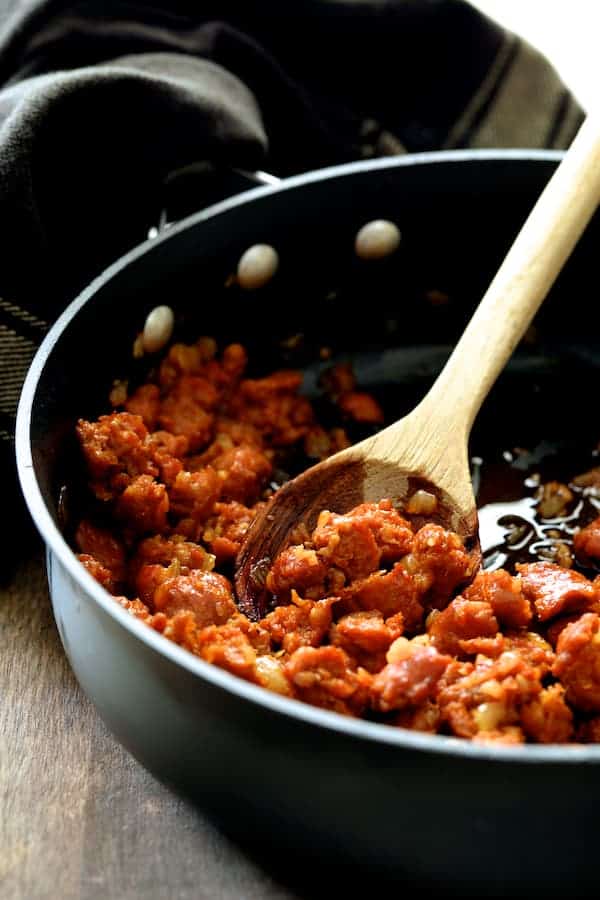Photo of chorizo being browned and stirred with wooden spoon in skillet.