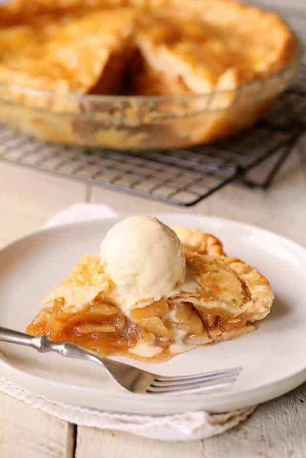 Slice of apple pie on white plate with vanilla ice cream.