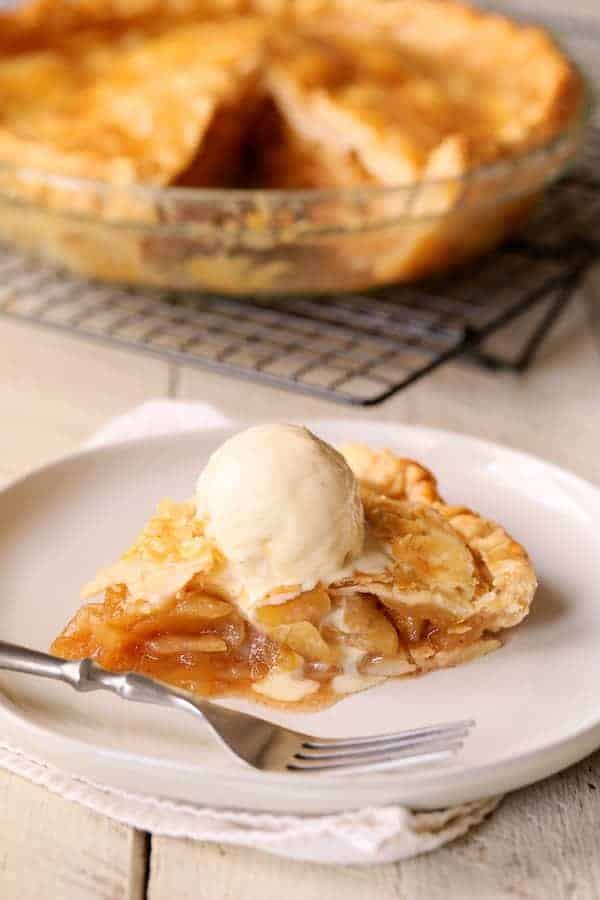 Photo of a slice of pie on white plate with vanilla ice cream and pie in the background.