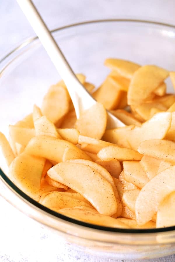 Photo of apples tossed with sugars and spices in glass bowl.