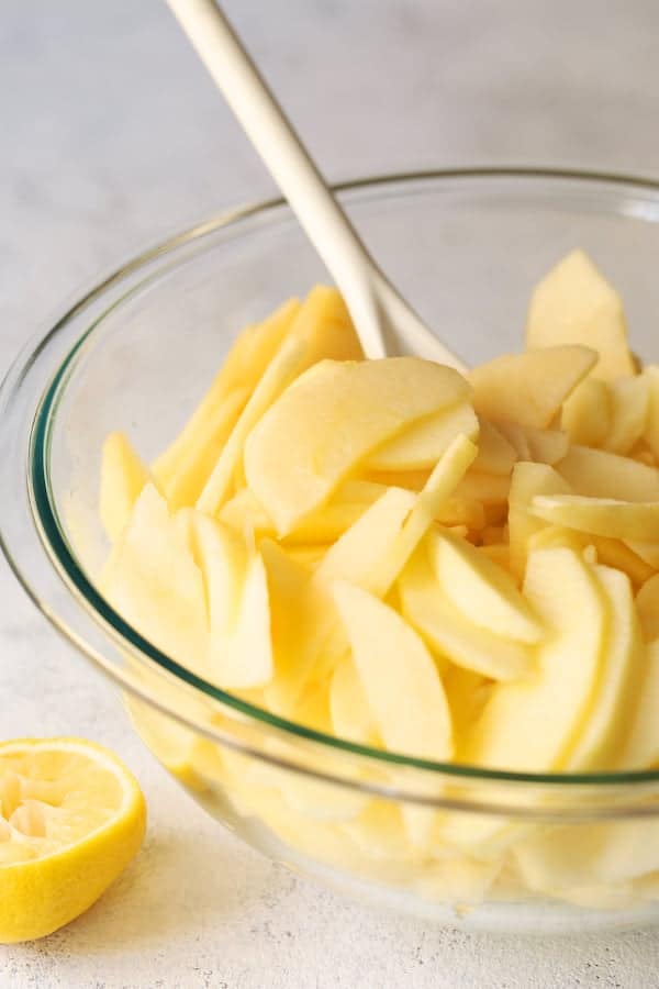 Photo of freshly sliced apples in glass bowl being stirred with white spoon.