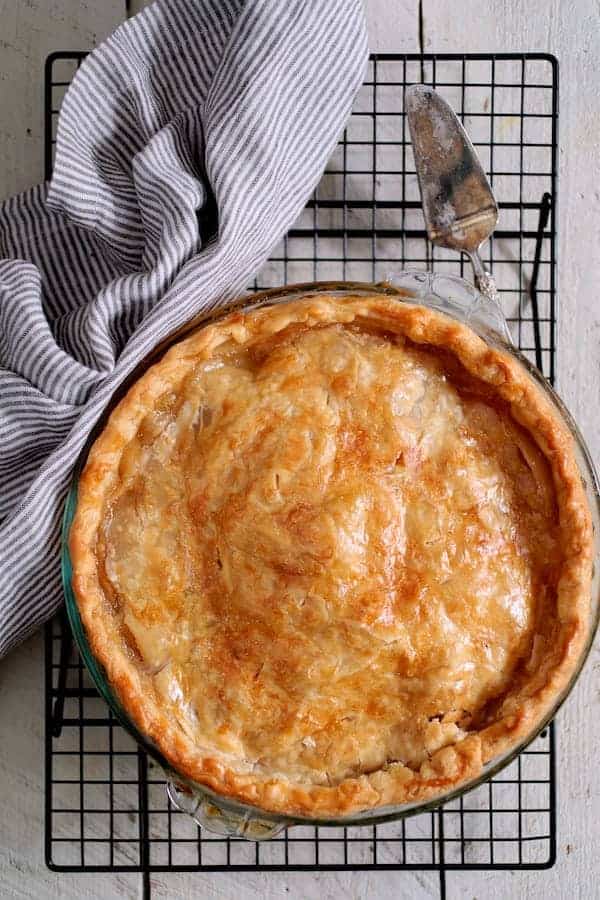 Photo of whole apple pie on cooling rack with gray striped towel.