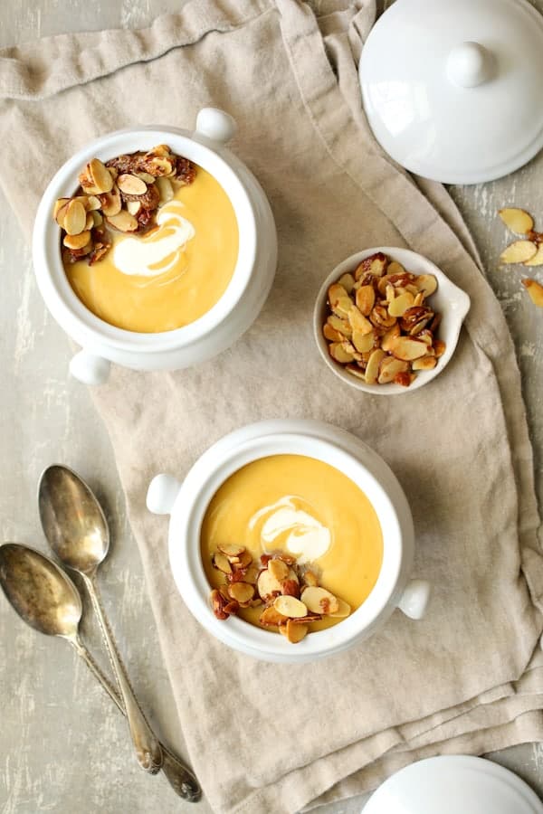 Photo of two servings of Pumpkin Soup with Marsala and Mascarpone in bowls on beige napkin with spoons and almond topping.