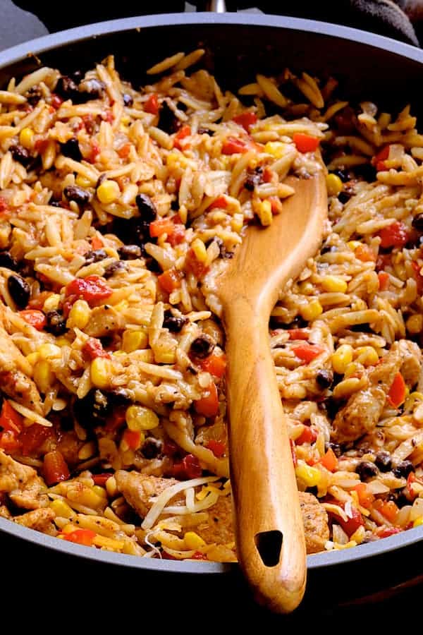 Close-up photo of Southwestern Chicken Orzo and Black Bean Skillet with wooden spoon.
