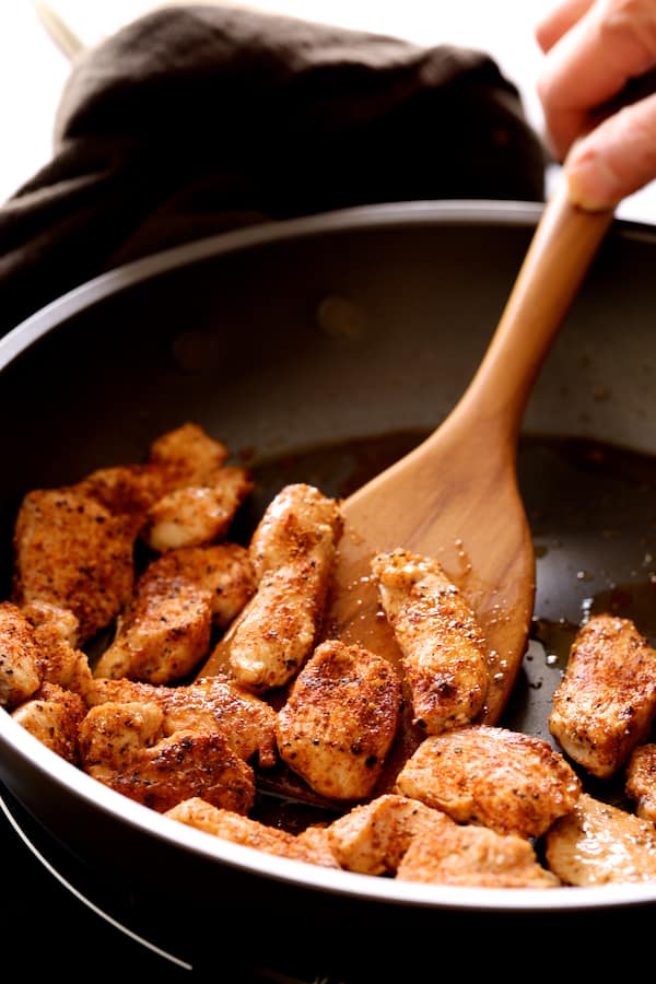 Photo of chicken in skillet being cooked and stirred with wooden spoon.