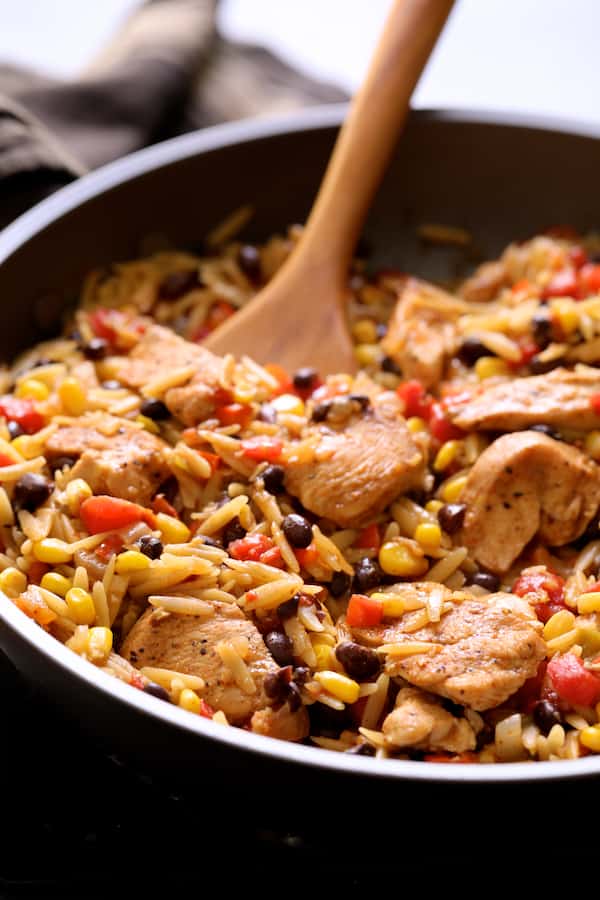 Close-up photo of Southwestern Chicken Orzo and Black Bean Skillet being stirred with wooden spoon.