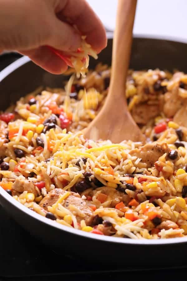 Photo of Southwestern Chicken Orzo and Black Bean Skillet with cheese being added.