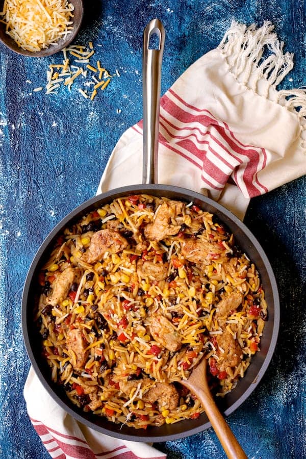 Photo of Southwestern Chicken Orzo and Black Bean Skillet on blue background with red and white striped towel.