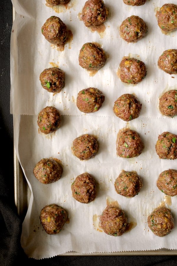 Photo of baked meatballs on parchment paper.