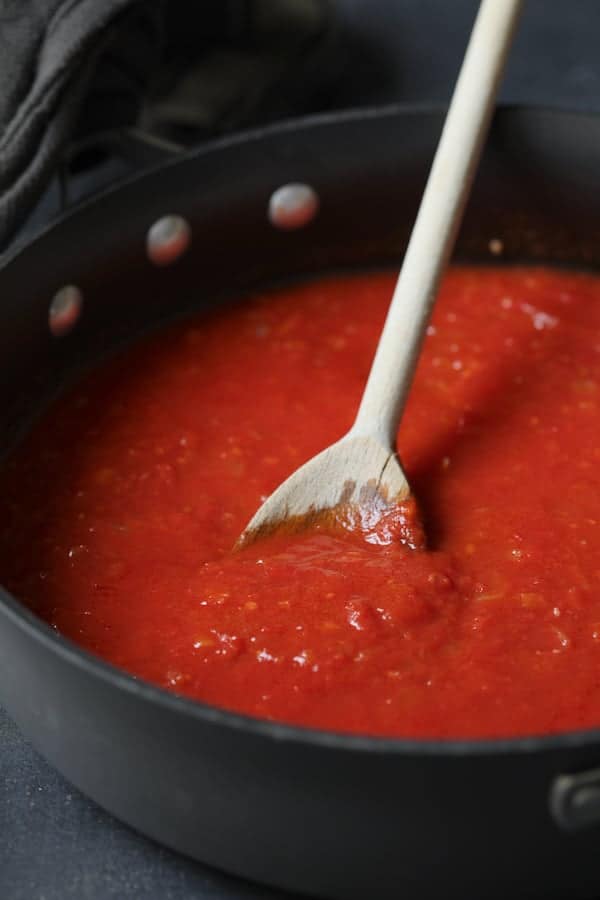 Photo of tomato sauce in skillet being stirred with wooden spoon.