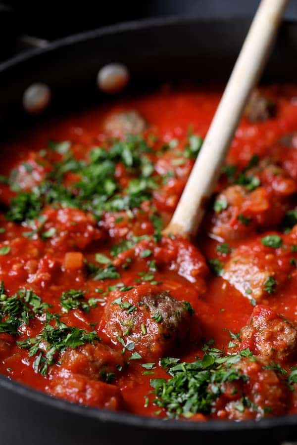 Photo of Middle Eastern Meatballs in Tomato Sauce in skillet being stirred with wooden spoon.