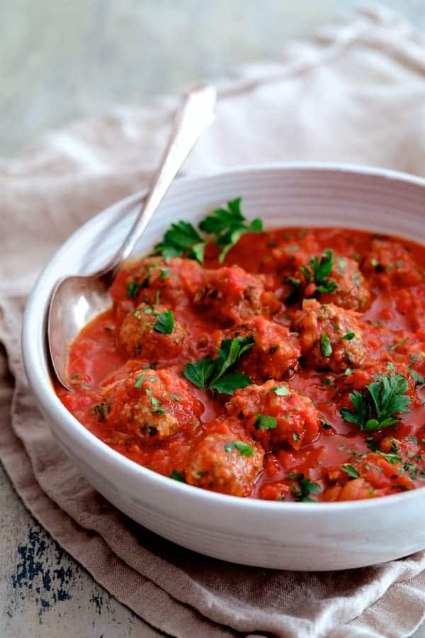 Photo of Middle Eastern Meatballs in Tomato Sauce in white serving bowl with serving spoon garnished with parsley.