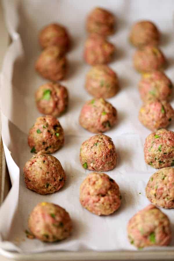 Photo of unbaked meatballs on parchment paper lined up in rows.