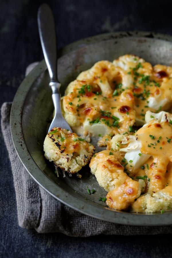 Close-up photo of Cauliflower Welsh Rarebit in metal dish with a piece on a fork.