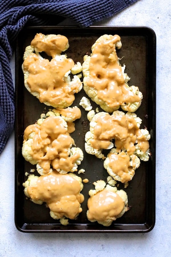 Photo of cauliflower steaks on baking sheet with cheese poured over them.