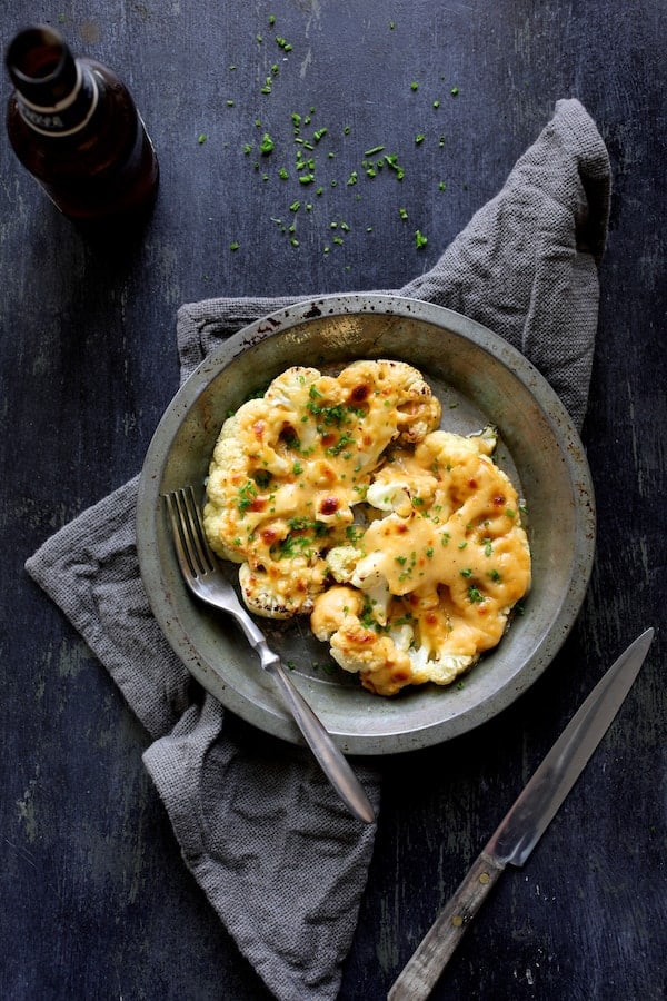 Photo of Cauliflower Welsh Rarebit in metal dish on blue background with gray napkin.