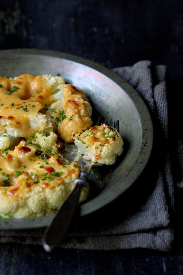 Close-up photo of Cauliflower Welsh Rarebit in metal baking dish with a piece of cauliflower on fork.