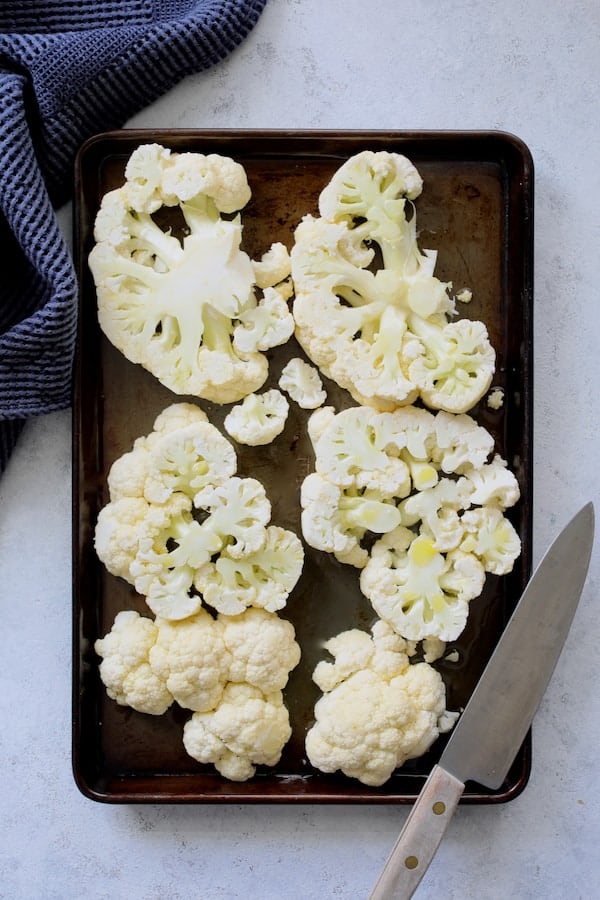 Photo of cauliflower steaks on baking sheet ready for roasting.
