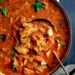 Old Fashioned Potato Cabbage and Kielbasa Soup - Overhead in white Dutch oven with ladle scooping out soup.