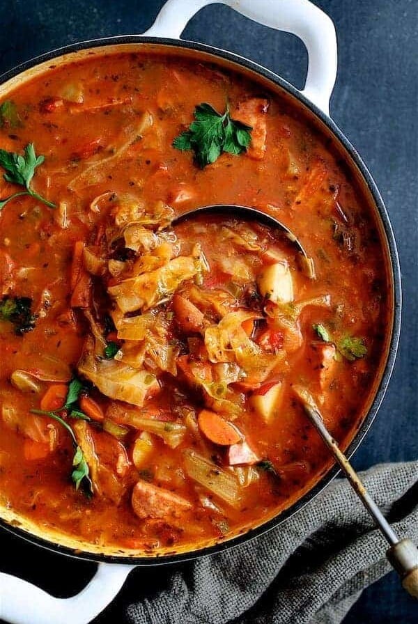 Old Fashioned Potato Cabbage and Kielbasa Soup - Overhead in white Dutch oven with ladle scooping out soup.